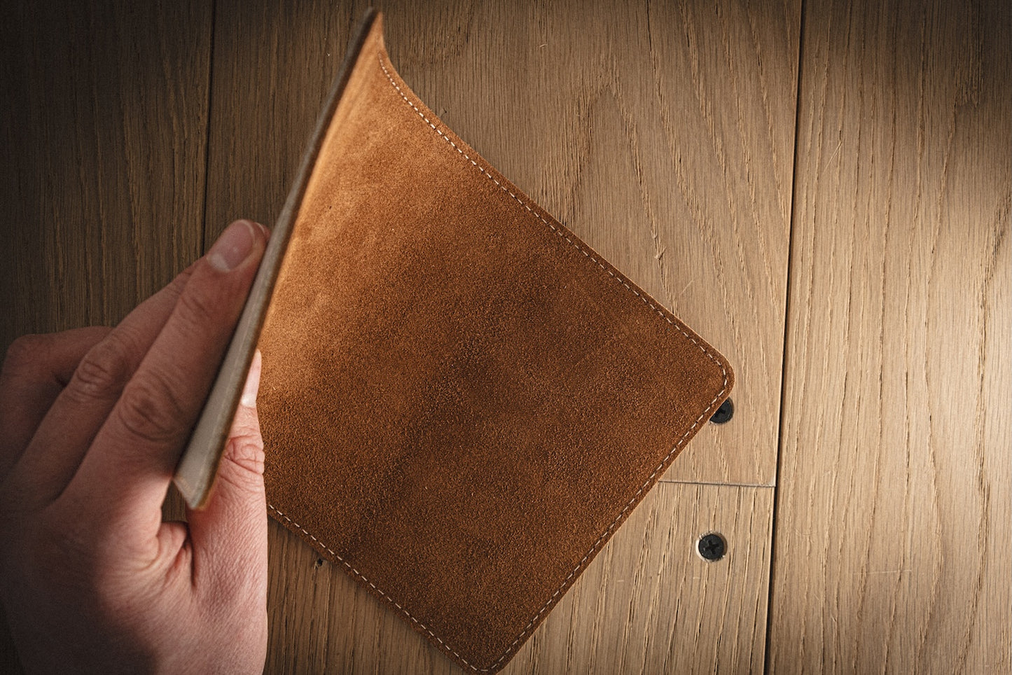 A person holds an open SAMPLE SALE Valet 13 * 23 cm grey saffiano leather wallet over a wooden table. The sleek accessory appears empty, showcasing the wood grain of the table clearly beneath it.