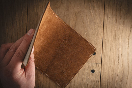 A person holds an open SAMPLE SALE Valet 13 * 23 cm grey saffiano leather wallet over a wooden table. The sleek accessory appears empty, showcasing the wood grain of the table clearly beneath it.