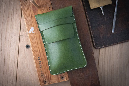 A SAMPLE SALE green, full leather pouch with white stitching rests on a wooden surface among dark brown leather pieces and metal tools, indicating a crafting environment ideal for personalization or creating sample pouches.