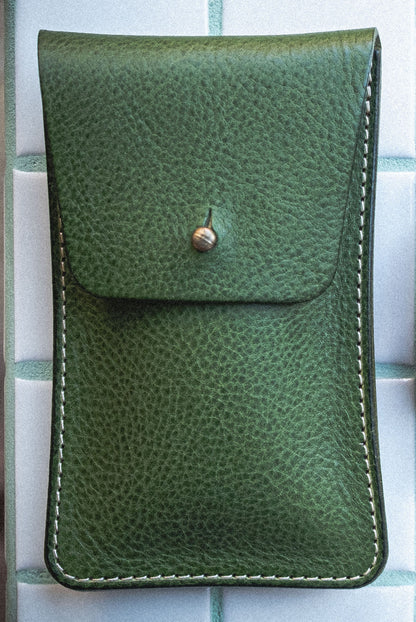The Pebbled Veg-Tan Collection "Vibrant" green leather pouch with a button snap closure is displayed upright against a white tiled background. Handmade in Antwerp, this pouch boasts visible white stitching along its edges, contributing both decorative appeal and durability.